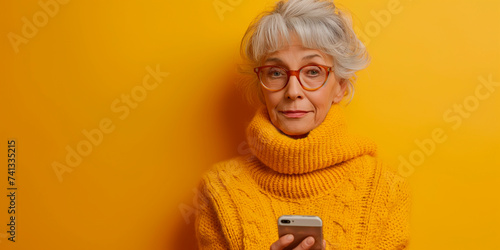 Portrait of mature lady in knit jumper confused using smartphone when someone stolen her privacy data isolated on yellow color background photo