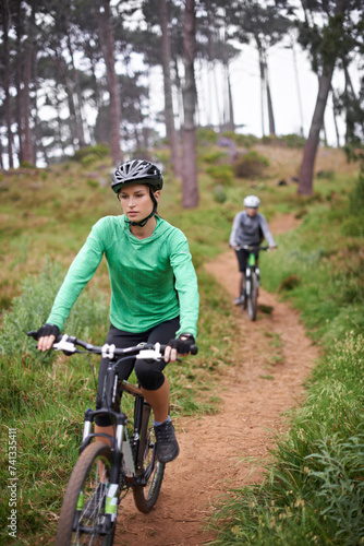 Woman, bike and cycling outdoor on trail for exercise, workout or adventure in forest with fitness. People, cyclists and bicycle with helmet in woods or off road for sport, hobby and travel in nature