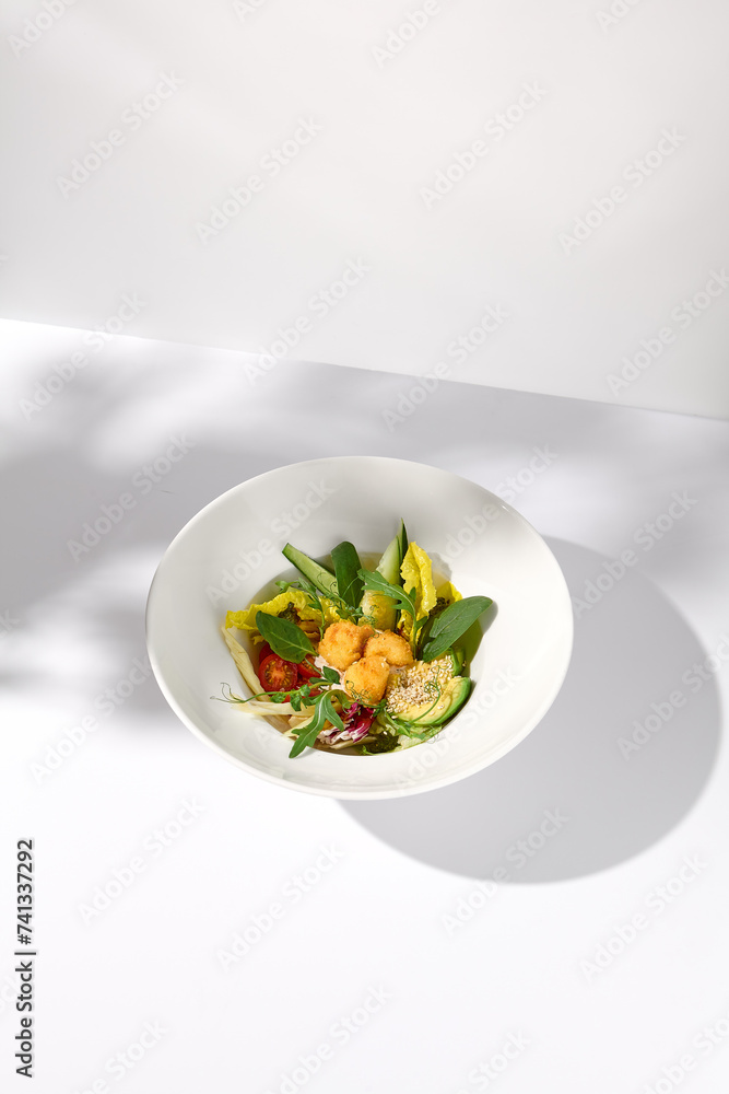 Vegetable salad bowl with avocado and cheese tempura balls, highlighted by shadows on a white surface Vegetable salad bowl with avocado and cheese tempura balls, highlighted by shadows on a white surface