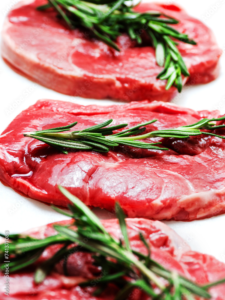 Three uncooked boneless lamb leg steak with fresh rosemary herb on white background. Premium high quality meat product of agriculture industry. Butcher craft and skill. Food supply chain.
