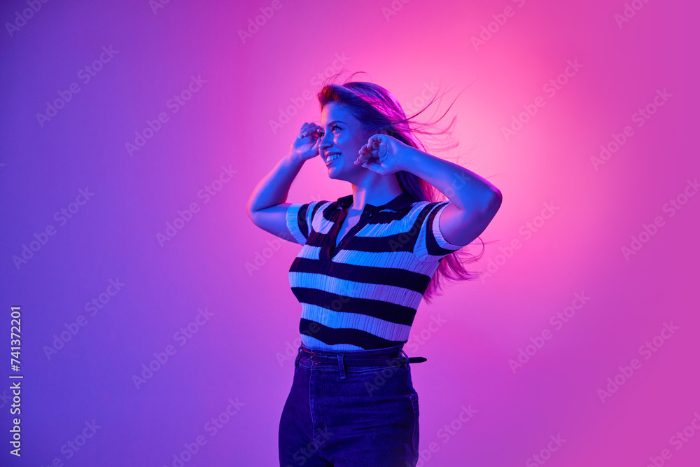 Gel portrait of attractive young woman smiling, posing in casual clothes against pink studio background in neon light. Happiness and joy. Concept of human emotions, youth, fashion, expression Gel portrait of attractive young woman smiling, posing in casual clothes against pink studio background in neon light. Happiness and joy. Concept of human emotions, youth, fashion, expression