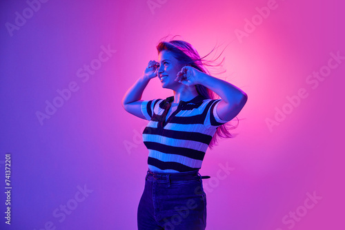 Gel portrait of attractive young woman smiling, posing in casual clothes against pink studio background in neon light. Happiness and joy. Concept of human emotions, youth, fashion, expression