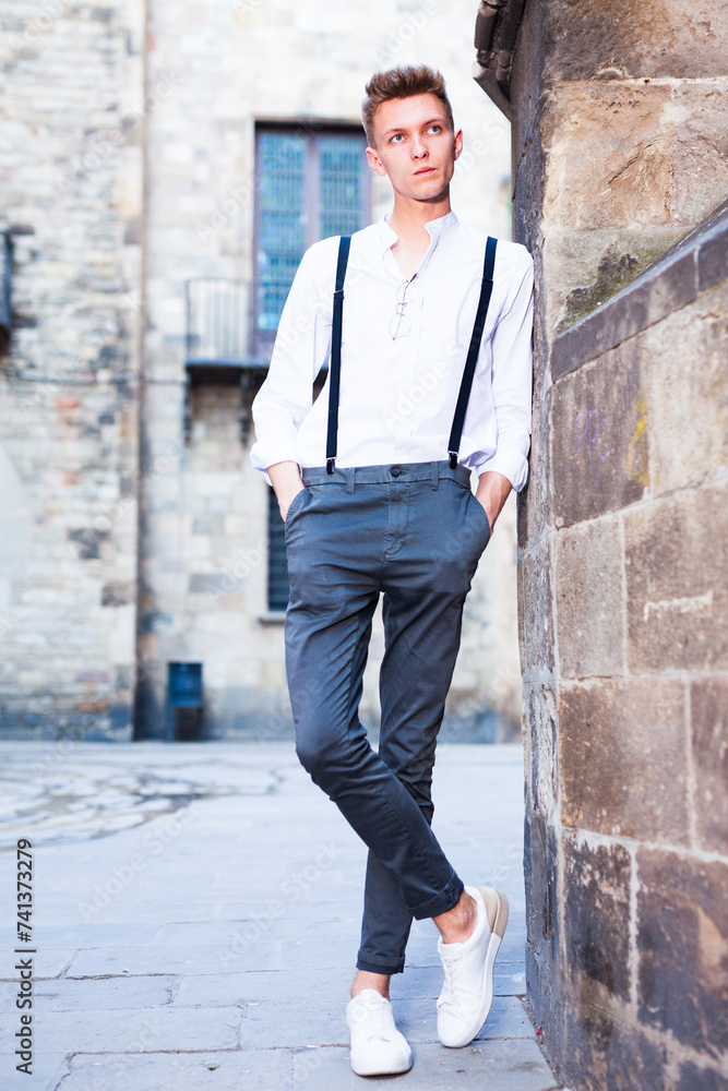 Young European guy in shirt and trousers with suspenders walking around city Young European guy in shirt and trousers with suspenders walking around city