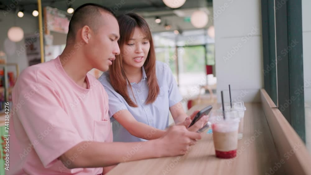 Two young male and female friends chatting and looking at smartphones in a coffee and burger shop.Happy lifestyle day Two young male and female friends chatting and looking at smartphones in a coffee and burger shop.Happy lifestyle day