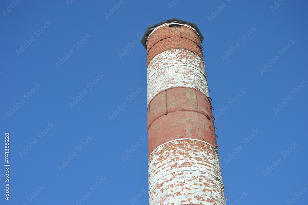 Round industrial red and white brick pipe against a blue sky.
