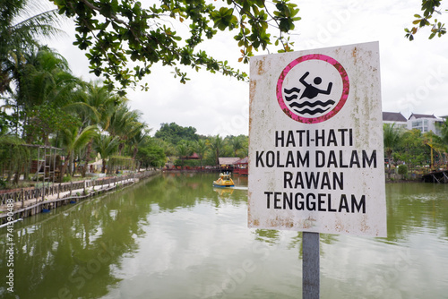 warning board with the words Hati hati kolam dalam rawan tenggelam in English, be careful, deep pools are prone to drowning photo