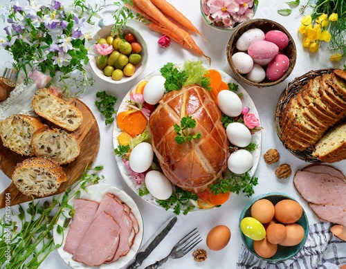 Traditional Easter dinner or brunch with ham, colored eggs, hot cross buns, cake and vegetables.