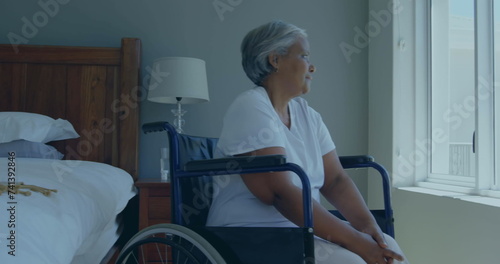 Senior biracial woman sits in a wheelchair at home, gazing outside