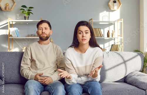 Family couple talking about relationship problems in online therapy. Young husband and wife sitting on couch in front of camera and discussing misunderstandings at virtual session with psychologist photo