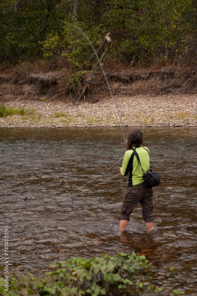 A woman in a green shirt is fishing by the river bank A woman in a green shirt is fishing by the river bank