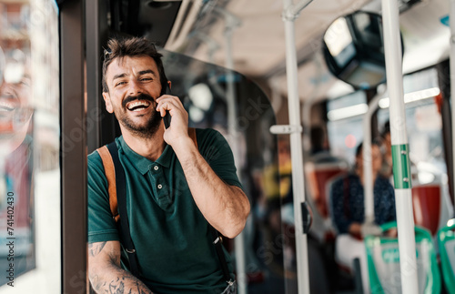 Portrait of a young happy man using public transportation and talking on the phone.