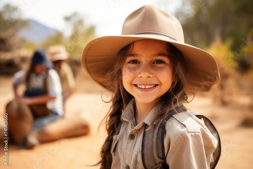 Cute little girl in cowboy hat looking at camera with her family on background © Nerea