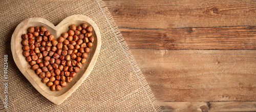 Hazelnuts in a heart-shaped plate on a wooden table and linen tablecloth. Hazelnuts background