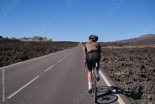 Man cyclist pedaling on road with view on mountain Teide volcano,Tenerife,Canary Islands,Spain. Sportsman training hard on bicycle outdoors.Sport motivation.Cycling training outdoors.Hipster cyclist.