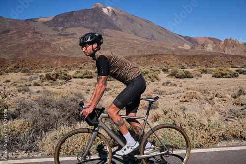 Fototapeta Naklejka Na Ścianę i Meble -  Male fit athlete riding time trial bicycle on empty road in golden hour. Sideview photo. Wearing helmet safety concept. Sport goal achieving. Extremely strong motivated person