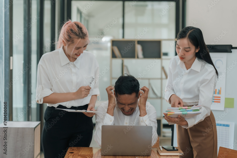 Stressed asian businessman with hands on head in a meeting as female colleagues discuss documents. Workplace stress and deadline pressure concept. Stressed asian businessman with hands on head in a meeting as female colleagues discuss documents. Workplace stress and deadline pressure concept.