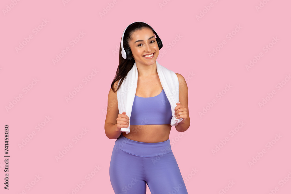 Happy athletic woman with towel and headphones on pink backdrop Happy athletic woman with towel and headphones on pink backdrop