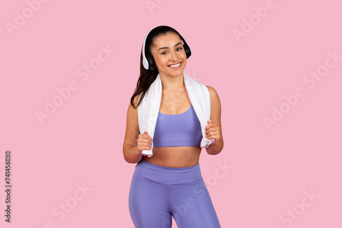 Happy athletic woman with towel and headphones on pink backdrop © Prostock-studio