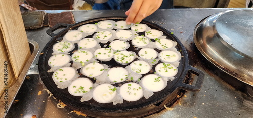 Khanom Krok Pan or Thai Coconut Pudding Pan filled with flour. The vendor is making khanom krok Traditional Thai desserts and sprinkling chopped green onions into the uncooked dough. Thai sweetmeat. 
