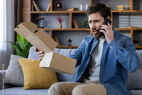 Frustrated man holding an empty cardboard box while talking on the phone