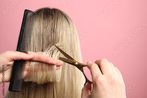 Hairdresser cutting client's hair with scissors on pink background, closeup. Space for text