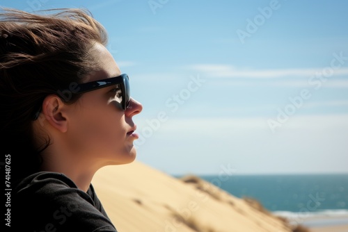 person with sunglasses looking out to sea from a dune