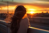 female with hair waves watching sunset from bridge