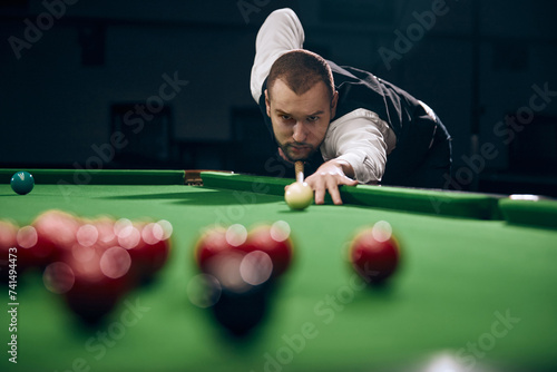 Schilderij op canvas Concentrated young man leaning on billiards table, playing snooker game