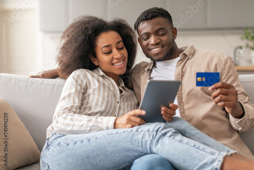 black couple enjoying shopping on tablet holding credit card indoors