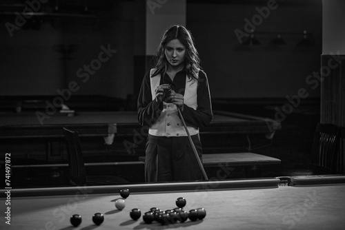 Tableau sur toile Young concentrated woman preparing cue with chalk over billiard table