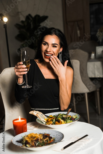 Luxurious woman in a black dress has dinner in a restaurant with flowers and a glass of champagne.Romantic dinner.International Women s Day concept
