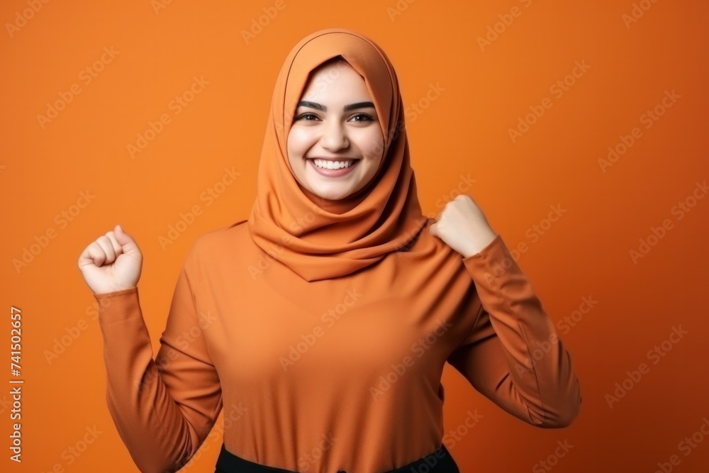 Beautiful young Muslim woman smiling confidently. Professional. Traditional looking camera pointing sideways on orange background. Beautiful young Muslim woman smiling confidently. Professional. Traditional looking camera pointing sideways on orange background.