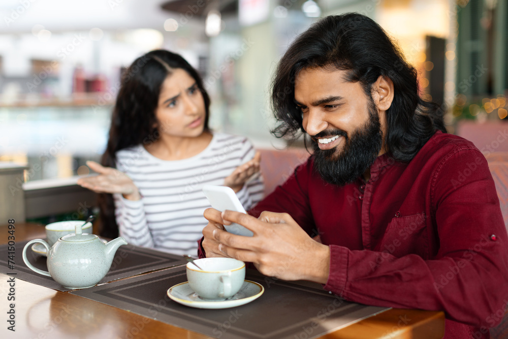 Angry young indian woman looking at boyfriend stuck in smartphone, Angry young indian woman looking at boyfriend stuck in smartphone,