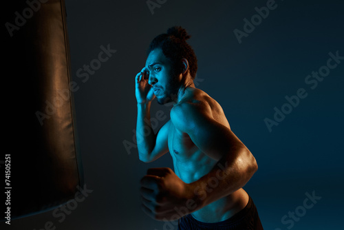 appealing shirtless african american man in black shorts punching actively boxing pear while in gym