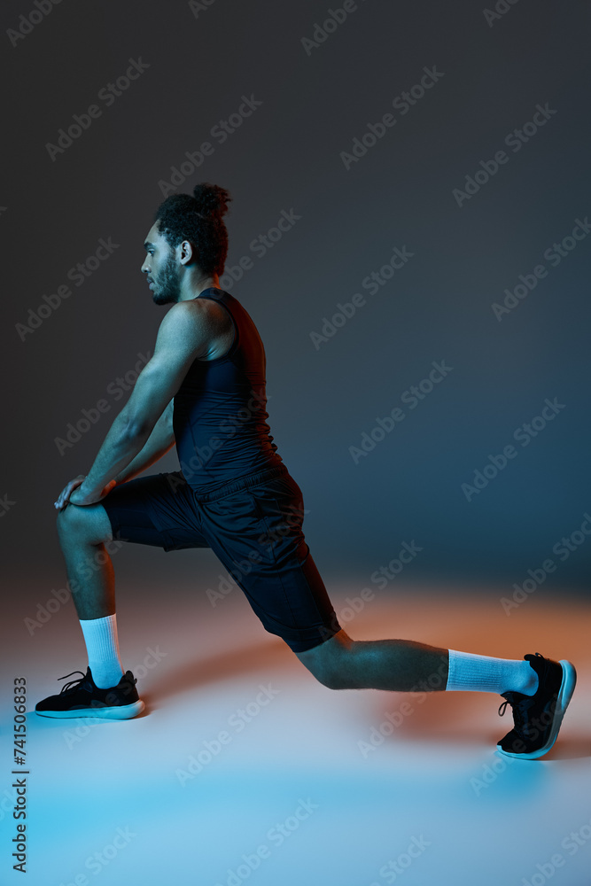 athletic handsome african american man in sportwear stretching muscles actively on dark backdrop