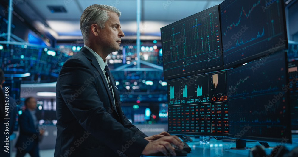 Fototapeta premium Portrait of Middle-Aged Stock Exchange Broker Working on a Computer with Multi-Screen Workstation with Real-Time Stocks, Commodities, Exchange Market Charts. Professional Investment Agent in Office
