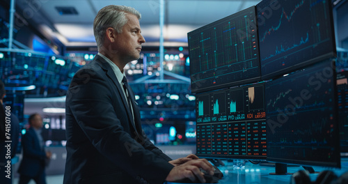 Portrait of Middle-Aged Stock Exchange Broker Working on a Computer with Multi-Screen Workstation with Real-Time Stocks, Commodities, Exchange Market Charts. Professional Investment Agent in Office
