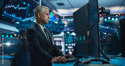 Portrait of Middle-Aged Stock Exchange Broker Working on Computer with Multi-Screen Workstation with Real-Time Stocks, Commodities and Exchange Market Charts. Professional Investment Agent in Office