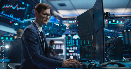 Portrait of Young Handsome Stock Exchange Broker Working on Computer, Researching Real-Time Stocks Data, Analyzing Commodities and Exchange Market Charts. Professional Investment Agent in Office