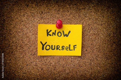 A yellow paper note with the phrase Know Yourself on it pinned to a cork board. Close up.