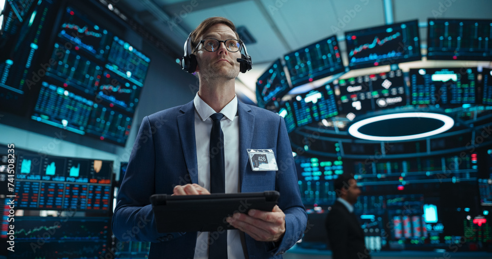 Fototapeta premium Portrait of a Young Handsome Stock Exchange Broker Using Tablet Computer, Researching Real-Time Stocks Data, Analyzing Commodities and Exchange Market Charts. Professional Investment Agent in Office