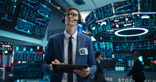 Portrait of a Successful Stock Exchange Manager Wearing Headphones, Working in Modern Office. Proactive Trader Browsing Internet on a Tablet Computer, Using Software with Stock Market Auctions