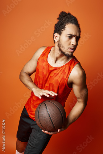 appealing young african american man in vibrant sport attire holding basketball on orange backdrop © LIGHTFIELD STUDIOS