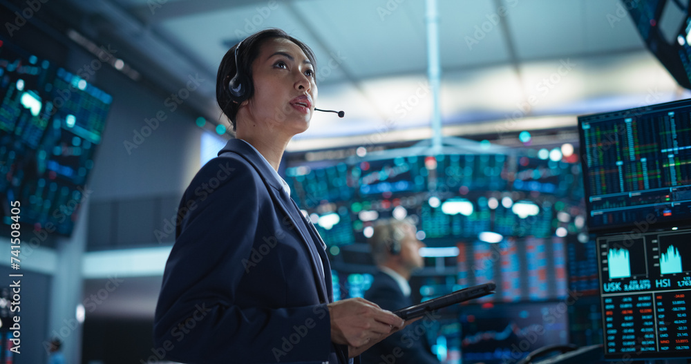 Successful Stock Exchange Manager Wearing Headphones, Working in Modern Office. Proactive Female Trader Browsing Financial Reports on a Tablet Computer, Using Software with Stock Market Auctions Successful Stock Exchange Manager Wearing Headphones, Working in Modern Office. Proactive Female Trader Browsing Financial Reports on a Tablet Computer, Using Software with Stock Market Auctions