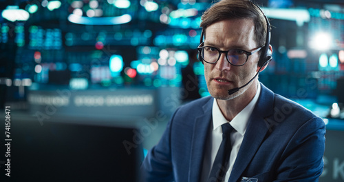 Close Up Portrait of a Smart and Thoughtful Stock Exchange Broker. Adult Man in Glasses Looking at Computer Screen, Communicating with a Client on a Phone Call, Talking About Investing Strategy