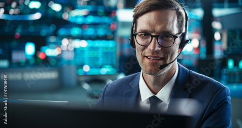 Close Up Portrait of a Smart and Thoughtful Stock Exchange Broker. Adult Man in Glasses Looking at Computer Screen, Communicating with a Client on a Phone Call, Talking About Investing Strategy