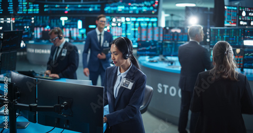 Female Stock Exchange Banker Working on a Desktop Computer with Real-Time Stocks, Commodities and Securities Market Charts. Professional Asian Investor Talking on a Mic with Business Partners