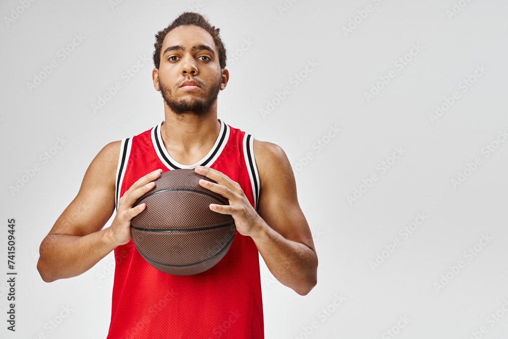 good looking african american man in sportwear holding basketball and looking straight at camera