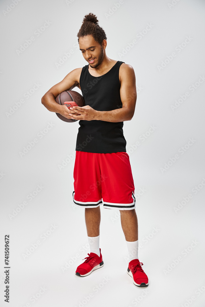 joyous appealing african american sportsman holding basketball and looking at phone, online betting joyous appealing african american sportsman holding basketball and looking at phone, online betting