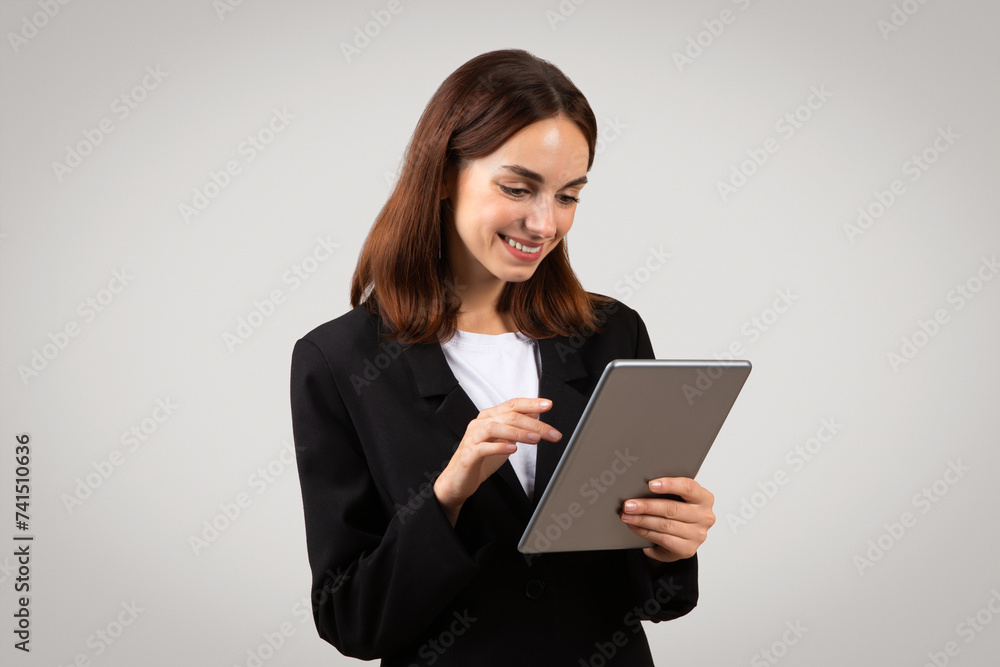 An attentive young businesswoman in a black blazer is focused on a tablet she's holding An attentive young businesswoman in a black blazer is focused on a tablet she's holding